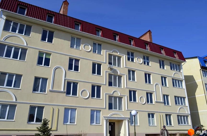 Фасад житлового комплексу Зелений гай з численними вікнами та червоним дахом. Будинок має чітку геометричну форму та декоративні елементи.