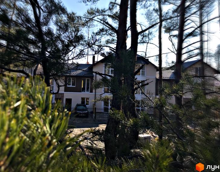 Котеджне містечко Сонячний 2: двоповерхові будинки з темним дахом, білими вікнами та коричневими елементами фасаду. На території видно припаркований автомобіль та зелені насадження.