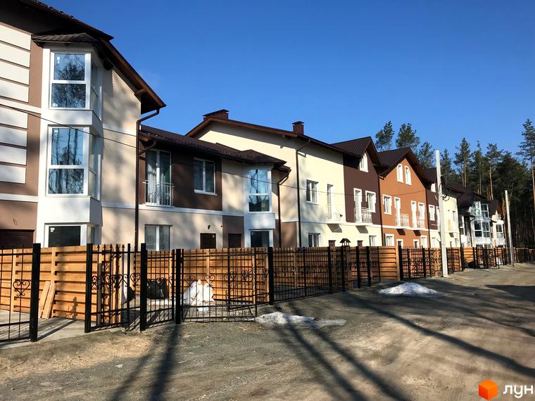 Котеджне містечко КМ Сонячний 2. Фасади будинків у світлих тонах з коричневими вставками, огороджена територія з дерев'яним парканом та кованими елементами.