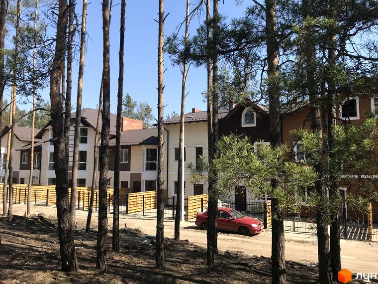 Котеджне містечко КМ Сонячний 2 - фасади будинків з коричневим дахом, білими та коричневими стінами, огороджена територія з дерев'яним парканом та червоним автомобілем.