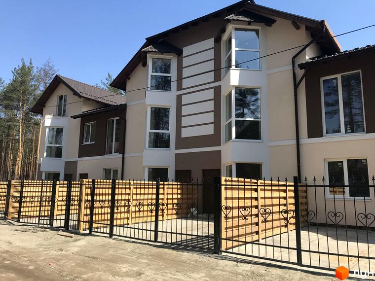 Котеджне містечко КМ Сонячний 2. Фасад будинку з великими вікнами, коричневими та бежевими елементами. Огороджена територія з дерев'яним парканом та кованими елементами.