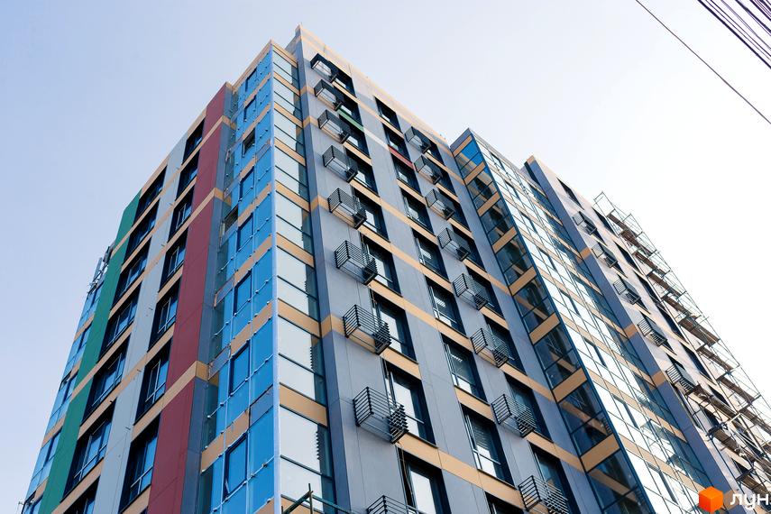 Новобудова Palermo з різнокольоровим фасадом, синіми скляними вікнами та металевими кошиками для кондиціонерів на сірих панелях.