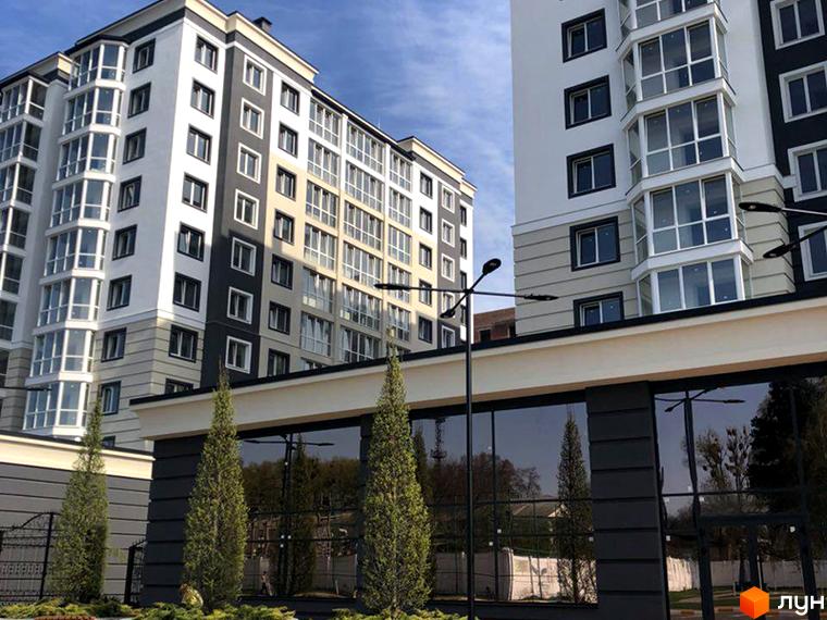 Високі будинки ЖК Continent з великими вікнами. На передньому плані рослини та огорожа з дзеркальним склом, що відображає навколишнє середовище.