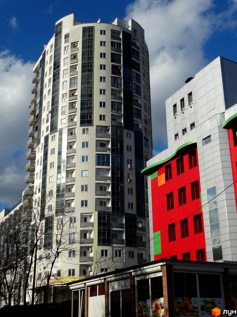 Житловий комплекс Аксіома – висотна будівля з панорамними вікнами та балконами. Поруч розташована новобудова з яскравим фасадом.