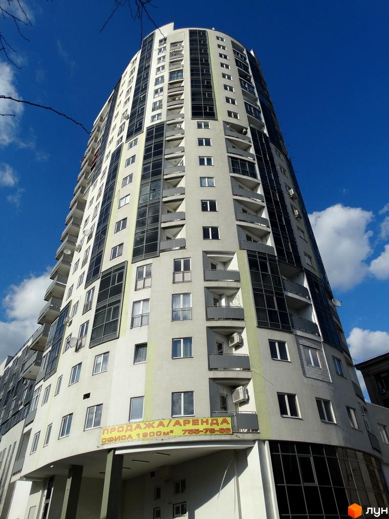 Житловий комплекс Аксіома – висотна будівля з вигнутим фасадом, балконами та панорамним склінням. На фасаді розміщена реклама продажу/оренди офісу.