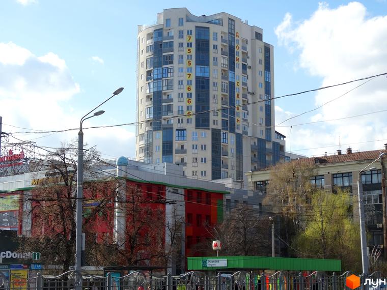 Високоповерховий житловий комплекс Аксіома з великою кількістю скління та балконів. Навколо будівлі видно дерева та міську забудову.