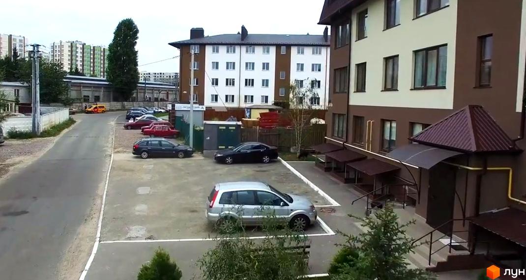 Зовнішній вигляд багатоповерхових будинків ЖК Оксамитовий з коричневими та білими фасадами. На прибудинковій території розташовані паркувальні місця та зелені насадження.