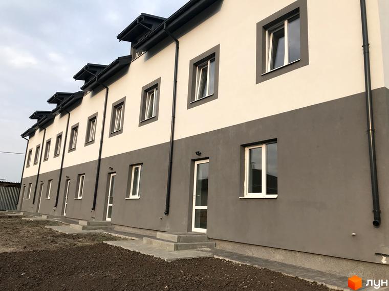 Ряд двоповерхових таунхаусів Таунхауси „HarmonyBud“ з двоколірним фасадом. Перед будинками ґрунт та вимощені доріжки.