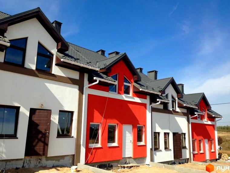 Зображення таунхаусів Grass House. Двоповерхові будинки з червоними та білими фасадами, сірими дахами. На передньому плані піщаний ґрунт.