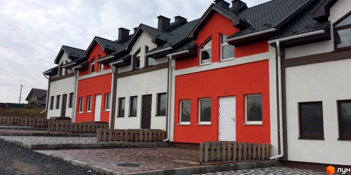 Зображення таунхаусів Grass House з червоними та білими фасадами, чорними дахами. Перед будинками викладена бруківка та встановлені декоративні дерев'яні огорожі.