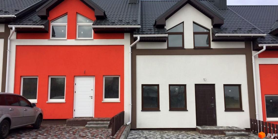 Таунхаус Grass House з червоним та білим фасадом, вікнами трикутної та прямокутної форми, біля будинку розташована прибудинкова територія з бруківкою та автомобілем.