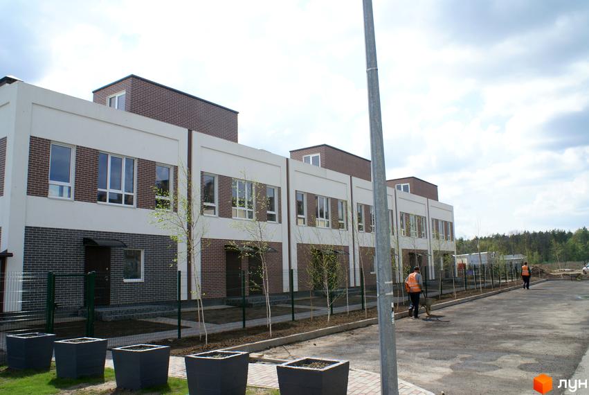 Житловий комплекс Кантрі Таунхаус: фасади будинків з цегляним оздобленням та білими елементами, прибудинкова територія з зеленими насадженнями та паркувальними місцями.