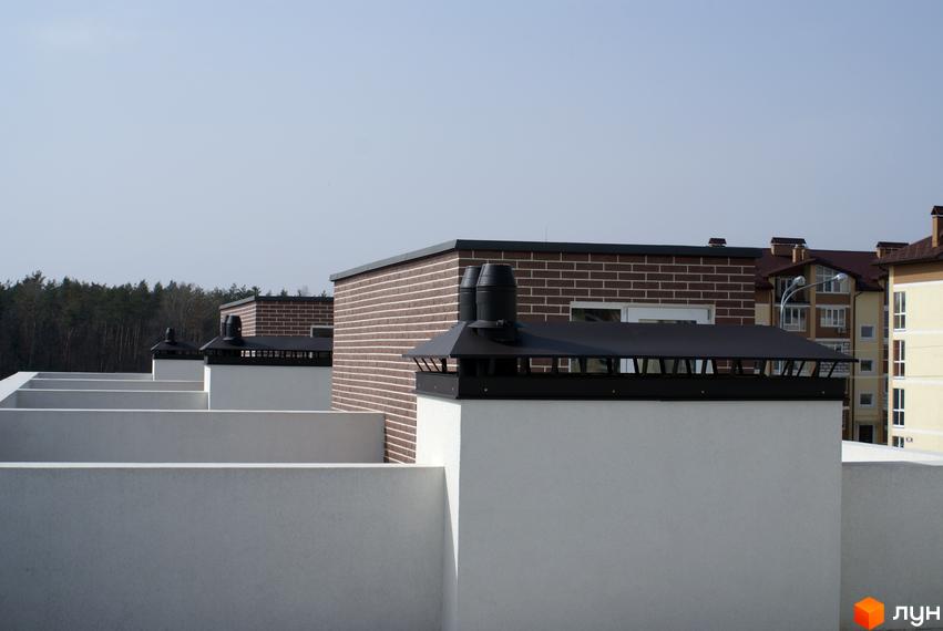 Зовнішній вигляд житлового комплексу Кантрі Таунхаус з цегляними фасадами та димоходами. Навколо видно інші будівлі та зелені насадження.