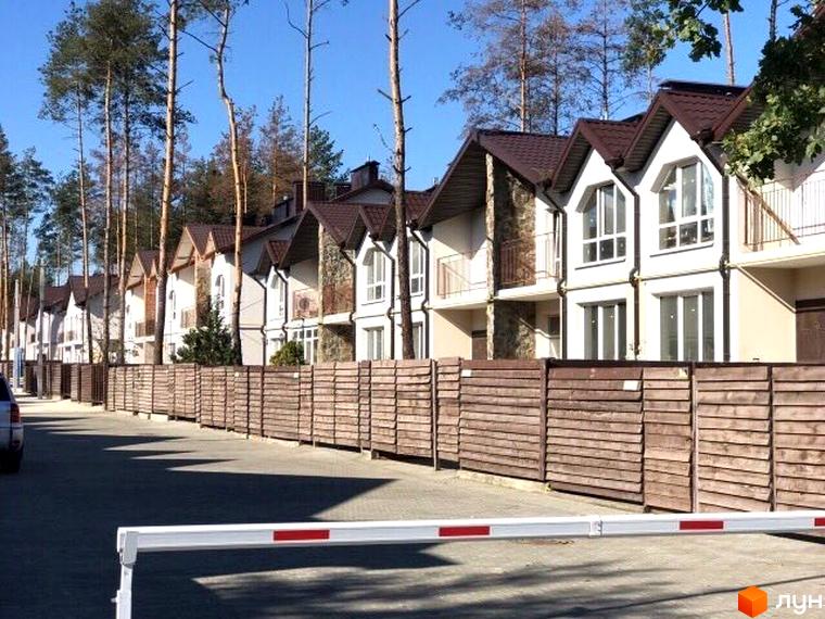 Таунхауси „Чеський двір“ – двоповерхові будинки з коричневими дахами та білими фасадами, розташовані вздовж дерев'яного паркану. На території комплексу видно зелені насадження та дорогу.