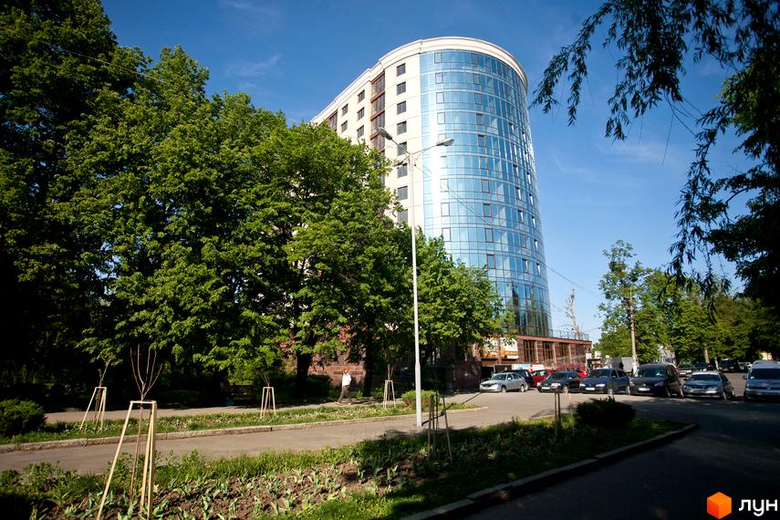 Зображення Житлового комплексу Paradise. Вигляд багатоповерхового будинку з панорамними вікнами та прилеглою територією з деревами та автомобілями.