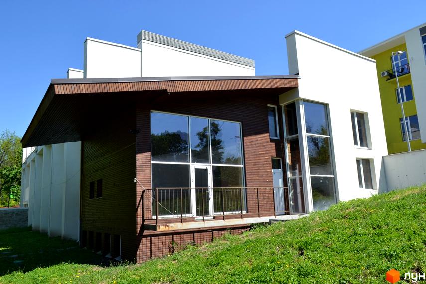 Зовнішній вигляд будинку Shatilovka Hillside з великими вікнами та дерев'яним фасадом. Навколо будинку зелена галявина з травою та квітами.