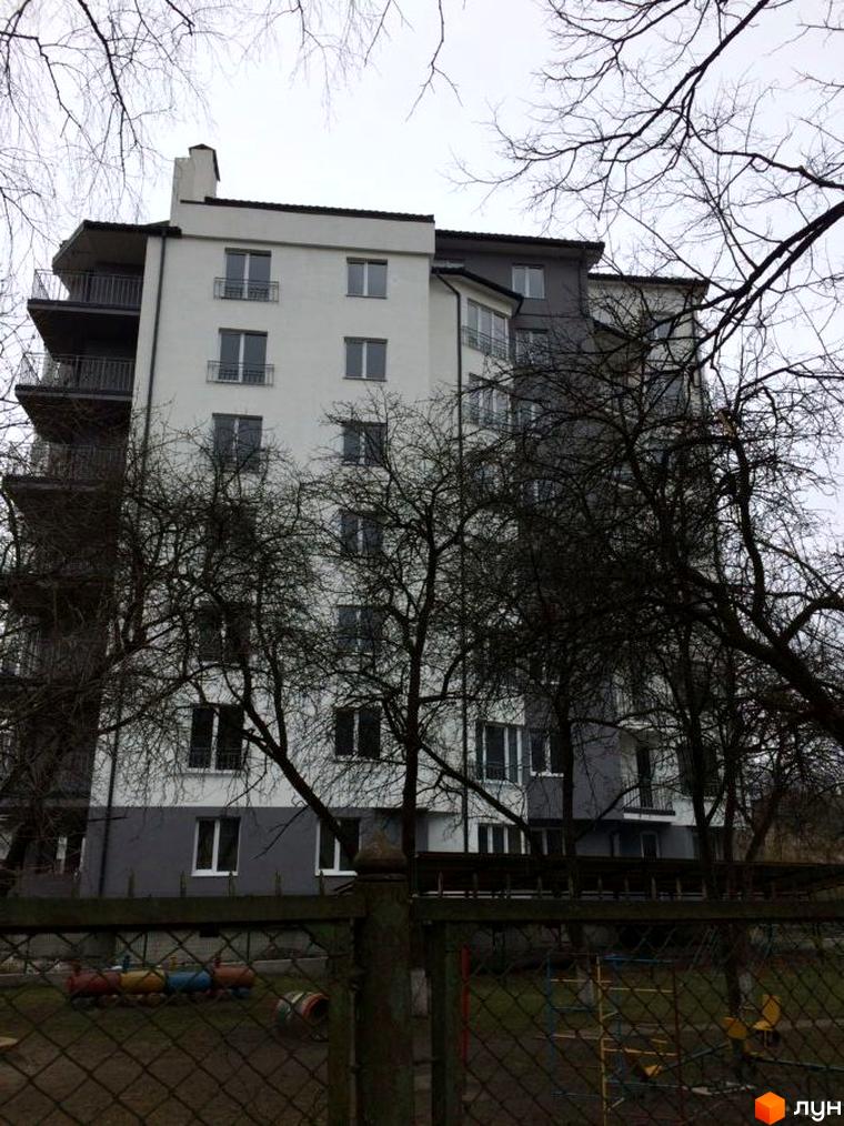 Житловий комплекс Гармонія. Зовнішній вигляд біло-сірої новобудови з балконами та вікнами. На прибудинковій території видно дитячий майданчик та паркан.
