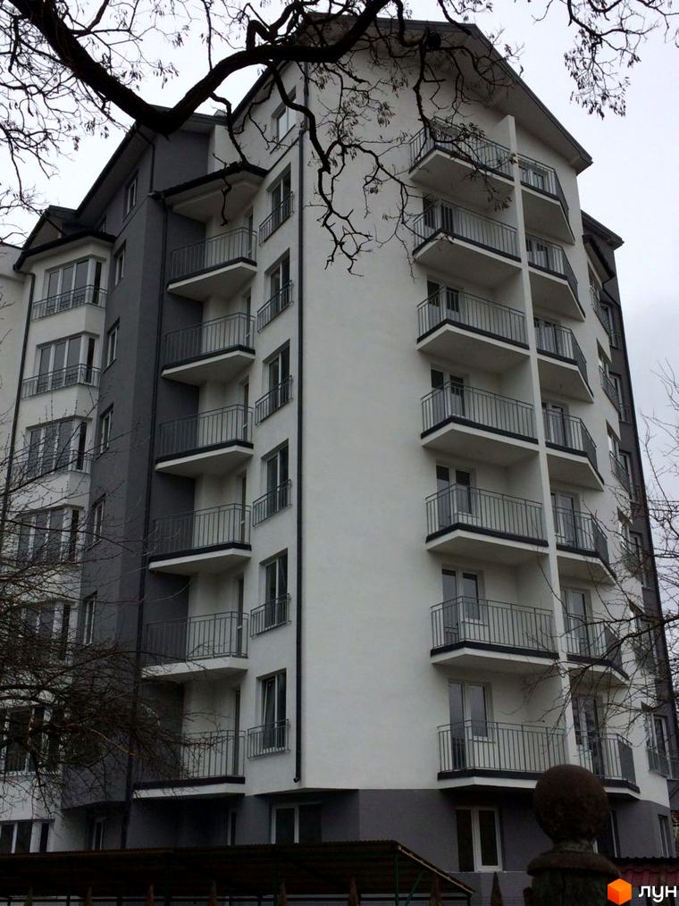 Фасад житлового комплексу Гармонія з численними балконами та вікнами. Будинок має сіро-біле оздоблення та металеві огорожі на балконах.