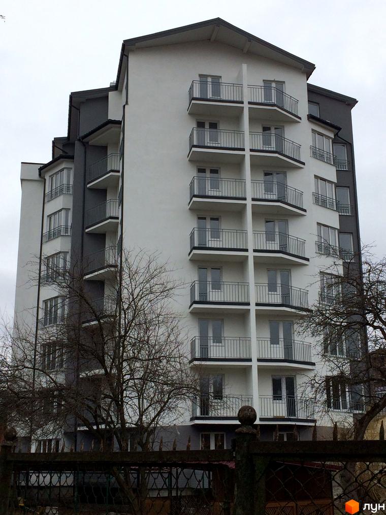 Зовнішній вигляд новобудови ЖК Гармонія з численними балконами та вікнами. Навколо будівлі видно голі дерева та паркан.