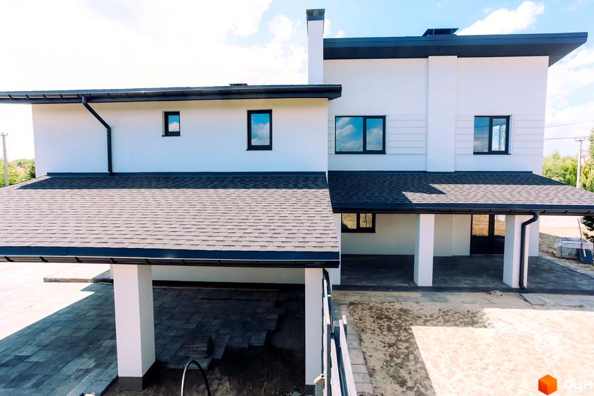 Білий двоповерховий будинок комплексу White Villages з темним дахом та навісом для авто. На прибудинковій території викладають бруківку.