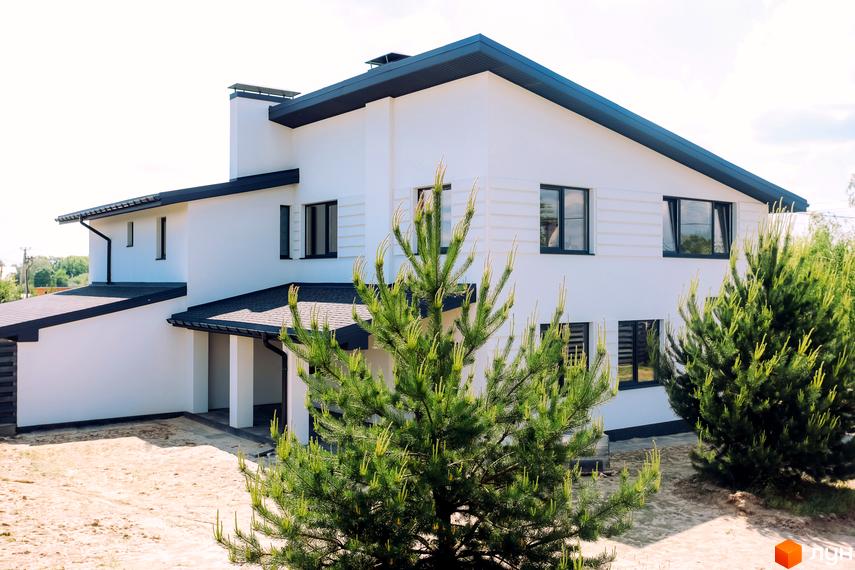 Сучасний білий дуплекс з темним дахом та вікнами. Навколо будинку піщана ділянка та зелені дерева.