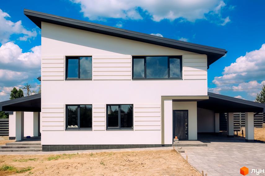 Сучасний двоповерховий будинок з великими вікнами та навісом для автомобіля. Зовнішній вигляд новобудови White Villages з прибудинковою територією під бруківкою.
