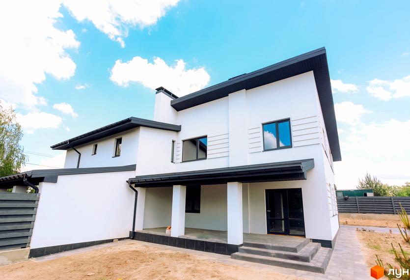 Сучасний двоповерховий будинок з білими стінами та темним дахом. Навколо будинку облаштована прибудинкова територія з бруківкою та парканом.