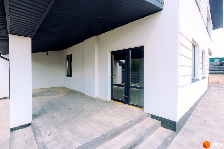 Зовнішній вигляд будинку з білими стінами, дверима та вікнами. Тераса з сірою плиткою та сходами.