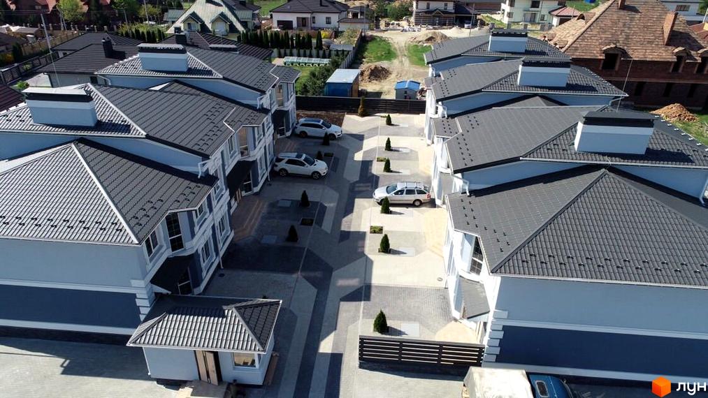 Котеджне містечко Чарівні Стежки: сірі дахи, світлі фасади будинків та доглянута прибудинкова територія з парковкою. Оглядовий вид на житловий комплекс.