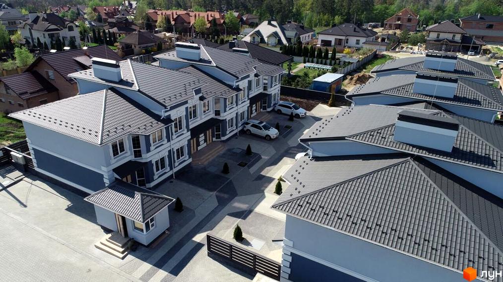 Котеджне містечко Чарівні Стежки. Сучасні будинки з сірими дахами та світлими фасадами, розташовані на доглянутій прибудинковій території з бруківкою та зеленими насадженнями.