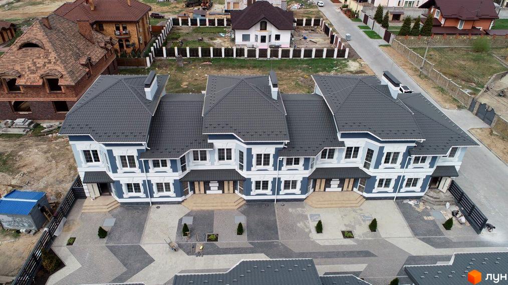 Котеджне містечко Чарівні Стежки: фасади будинків у синьо-білих кольорах, покрівля темного кольору, облаштована прибудинкова територія з бруківкою та зеленими насадженнями.