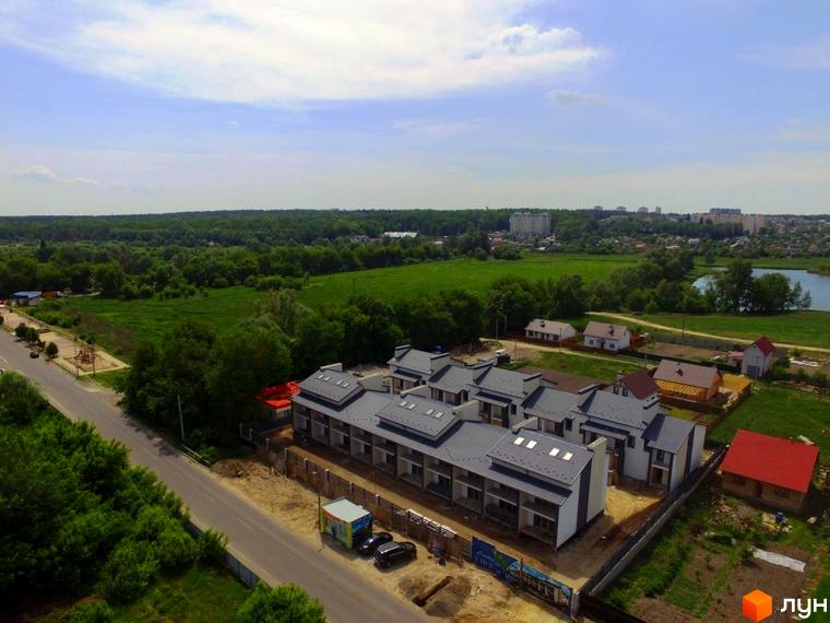 Будівельний проєкт Таунхаус „Мальовничий“ з сірими дахами та білими фасадами. Навколо зелена територія з деревами та дорогою.