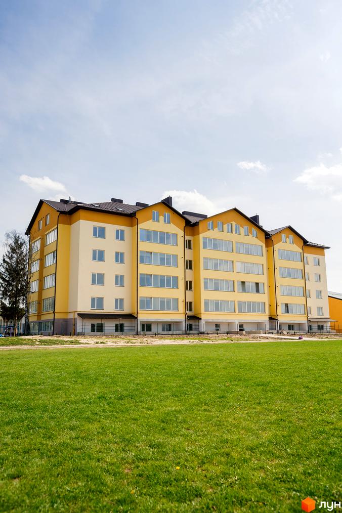 Житловий комплекс Сімейна Фортеця - жовта багатоповерхівка з великими вікнами на тлі блакитного неба. Попереду зелений газон.