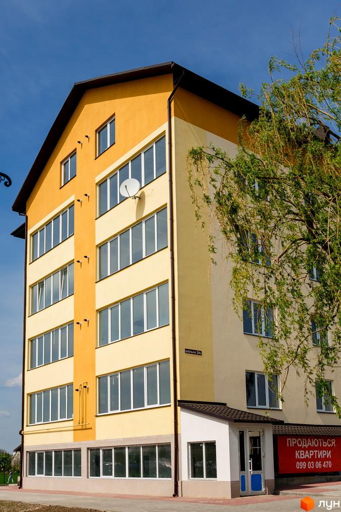 Зовнішній вигляд триповерхової новобудови ЖК Сімейна Фортеця з жовтим та світло-жовтим фасадом, великими вікнами та червоним банером 