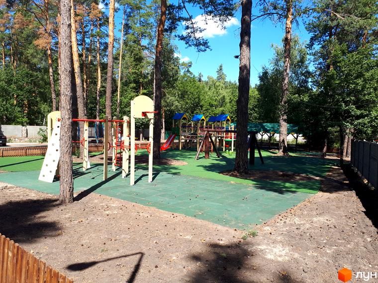 Дитячий майданчик у житловому комплексі Green Wood club з гірками та спортивними елементами, оточений зеленими насадженнями.
