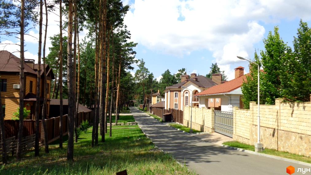 Фото Котеджного містечка Green Wood club: двоповерхові будинки з коричневими дахами та цегляними стінами, зелені газони та дерева вздовж дороги.