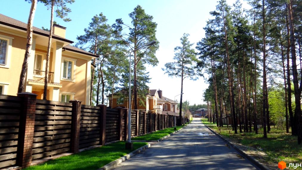Фото Котеджного містечка Green Wood club з виглядом на будинок та дорогу. Навколо сосни та зелений газон.