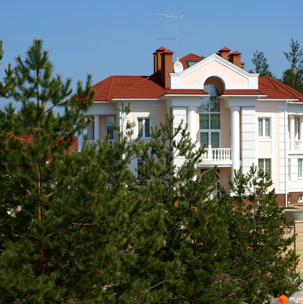 Зображення будинку в Котеджному містечку Green Wood club з червоним дахом та великими вікнами. Навколо сосни та доглянута територія.