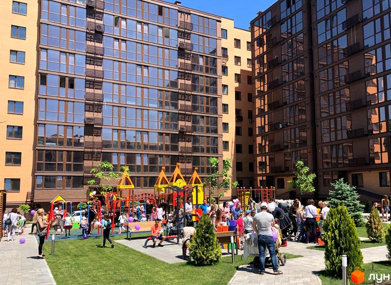 Житловий комплекс Атмосфера. Зовнішній вигляд будівель з великою кількістю скління та дитячий майданчик з зеленими насадженнями на прибудинковій території.
