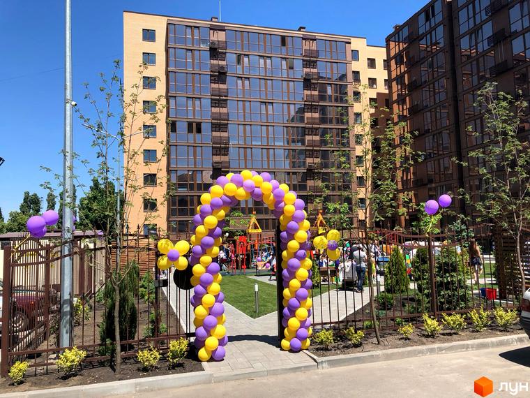 Житловий комплекс Атмосфера. Сучасна новобудова з жовто-фіолетовими повітряними кулями біля входу. Зелена прибудинкова територія з дитячим майданчиком.