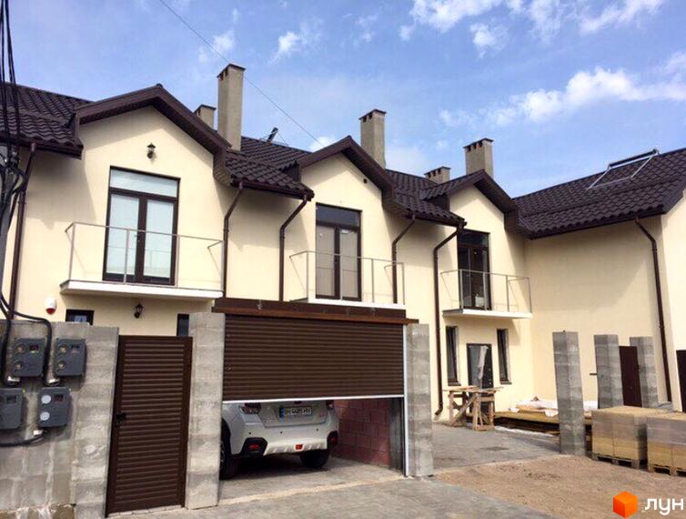 Таунхаус „Царське село“: фасади бежевого кольору, коричневі дахи та балкони. На території видно гараж, браму та будівельні матеріали.