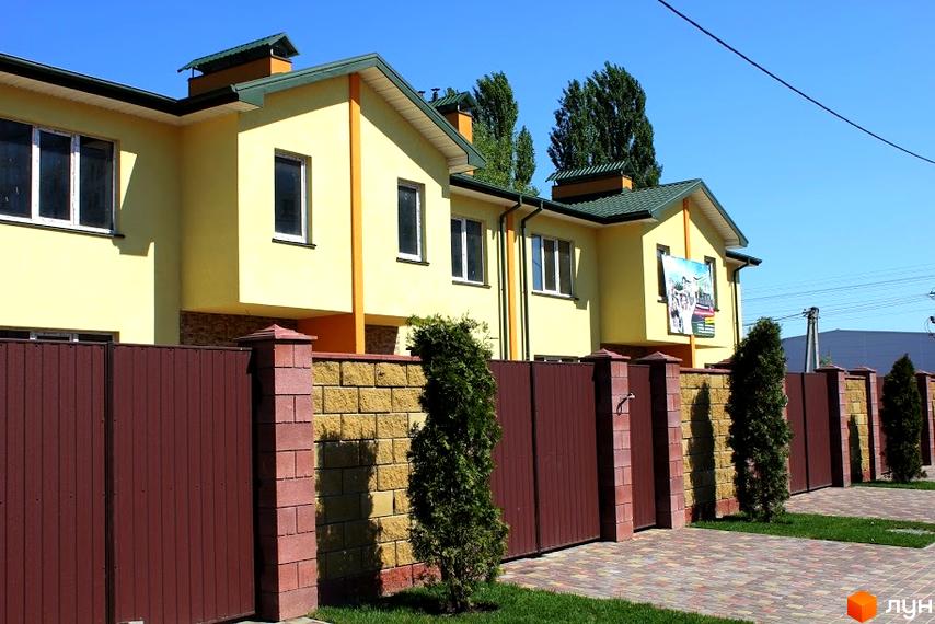 Зображення фасаду та огорожі Житлового комплексу по вул. Академіка Шалімова, 68/1а-68/1д. На передньому плані зелені насадження та тротуарна плитка.