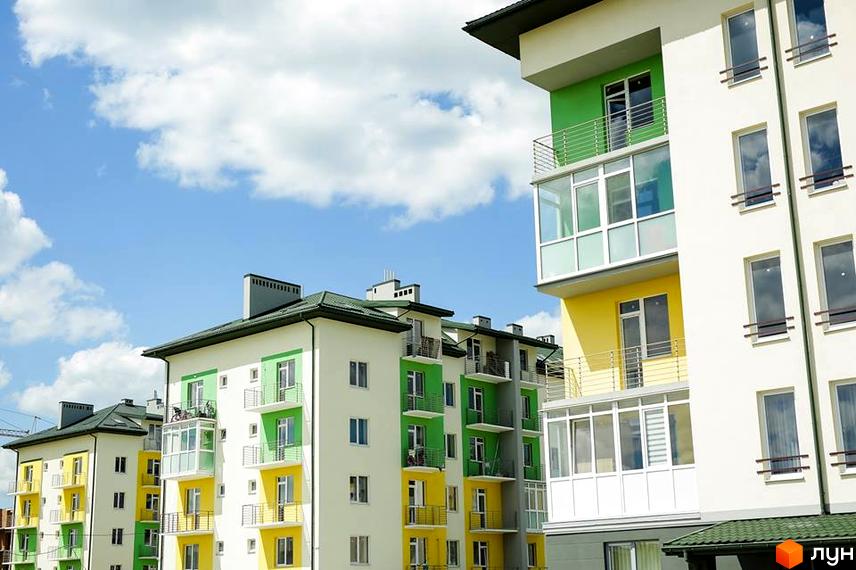 Багатоповерхові будинки Житлового комплексу Південний з білими, зеленими та жовтими фасадами, зеленими дахами та балконами. На тлі блакитного неба.