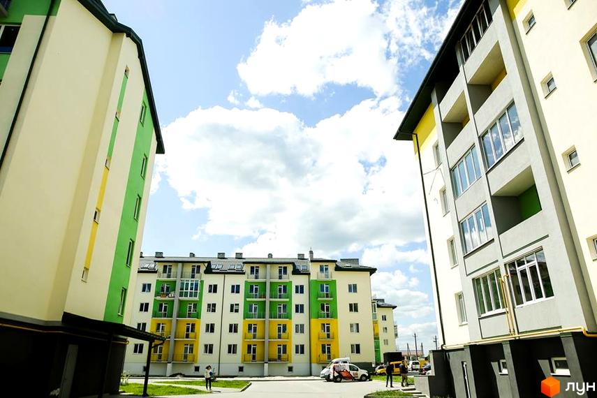 Новобудова Південний з багатоповерховими будинками, жовтими та зеленими фасадами. Прибудинкова територія має асфальтовані доріжки та зелені насадження.