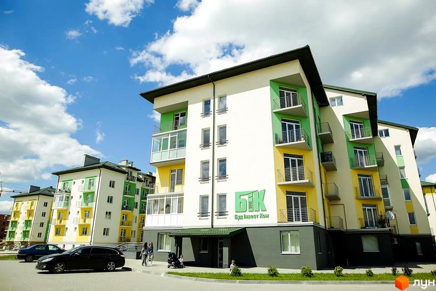 Житловий комплекс Південний: багатоповерхові будинки з білими, жовтими та зеленими фасадами, обладнані балконами. На прибудинковій території є дорога, зелені насадження та пішоходи.