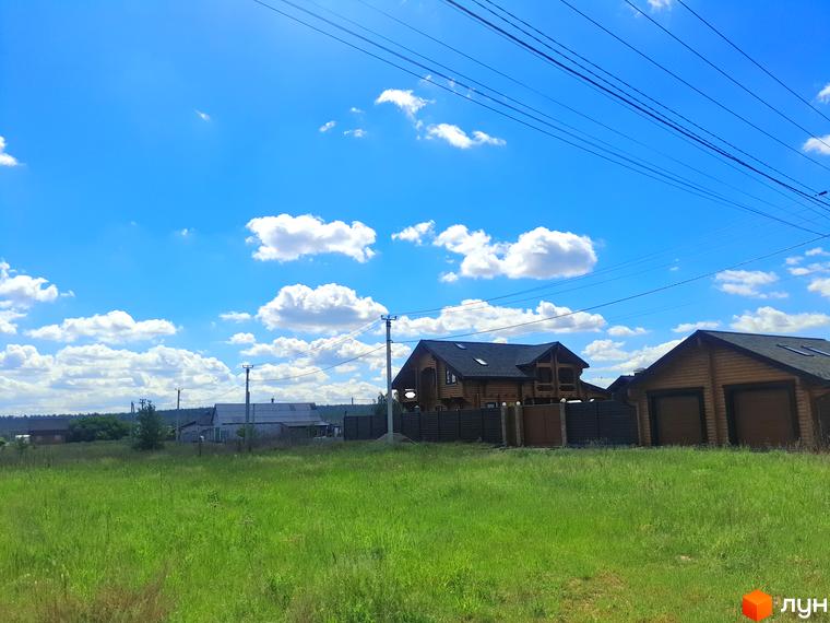 Дерев'яний будинок з темним дахом на тлі блакитного неба з хмарами. На передньому плані зелена трава.