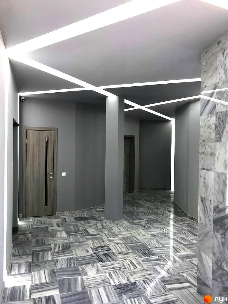 Інтер'єр холу в ЖК Миконос. Сірі стіни, підлога з мармурової плитки, світлодіодне освітлення на стелі. Вид на вхідні двері та коридор.