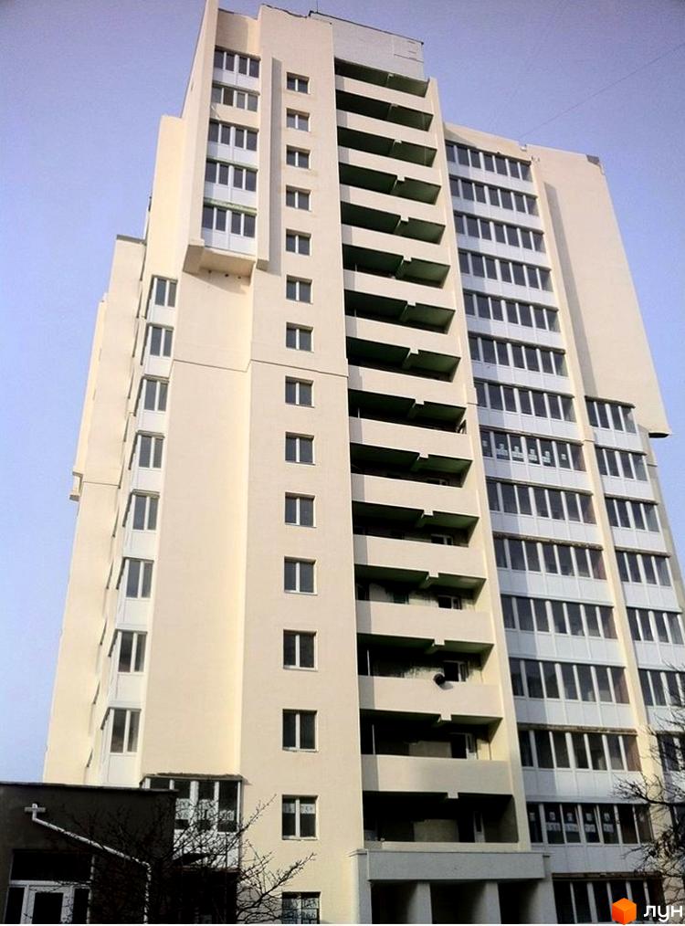 Висотна будівля житлового комплексу з численними вікнами та балконами. На передньому плані видно частину прибудинкової території.