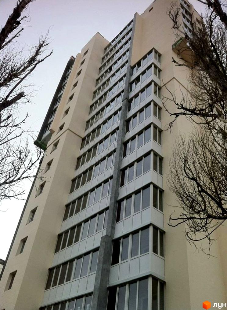 Висотна будівля житлового комплексу з великою кількістю вікон. Навколо будівлі видно дерева без листя.