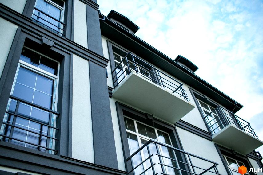 Фасад Клубного будинку Giverny HOUSE: світлі стіни, темні декоративні елементи навколо вікон та балкони з чорними металевими поручнями.